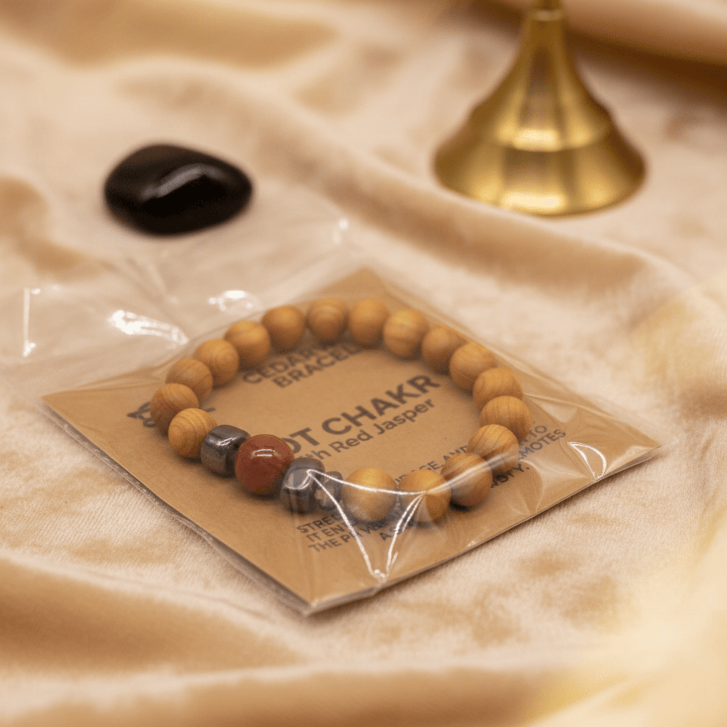 Bracelet en cèdre et jaspe rouge emballé sur carte kraft chakra racine, posé sur tissu beige.