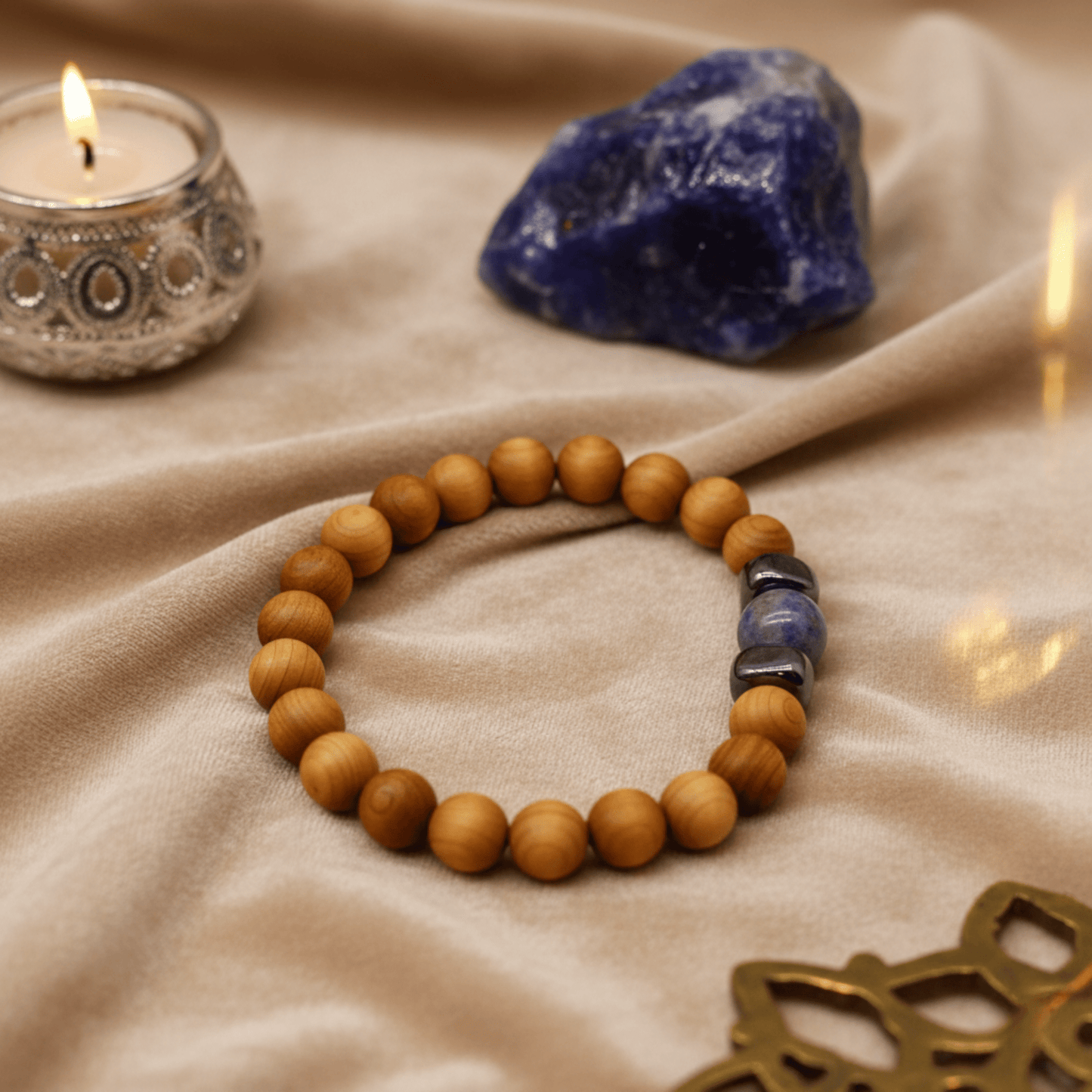 Bracelet en cèdre et sodalite mis en scène avec bougie argentée et pierre bleue sur tissu doux.