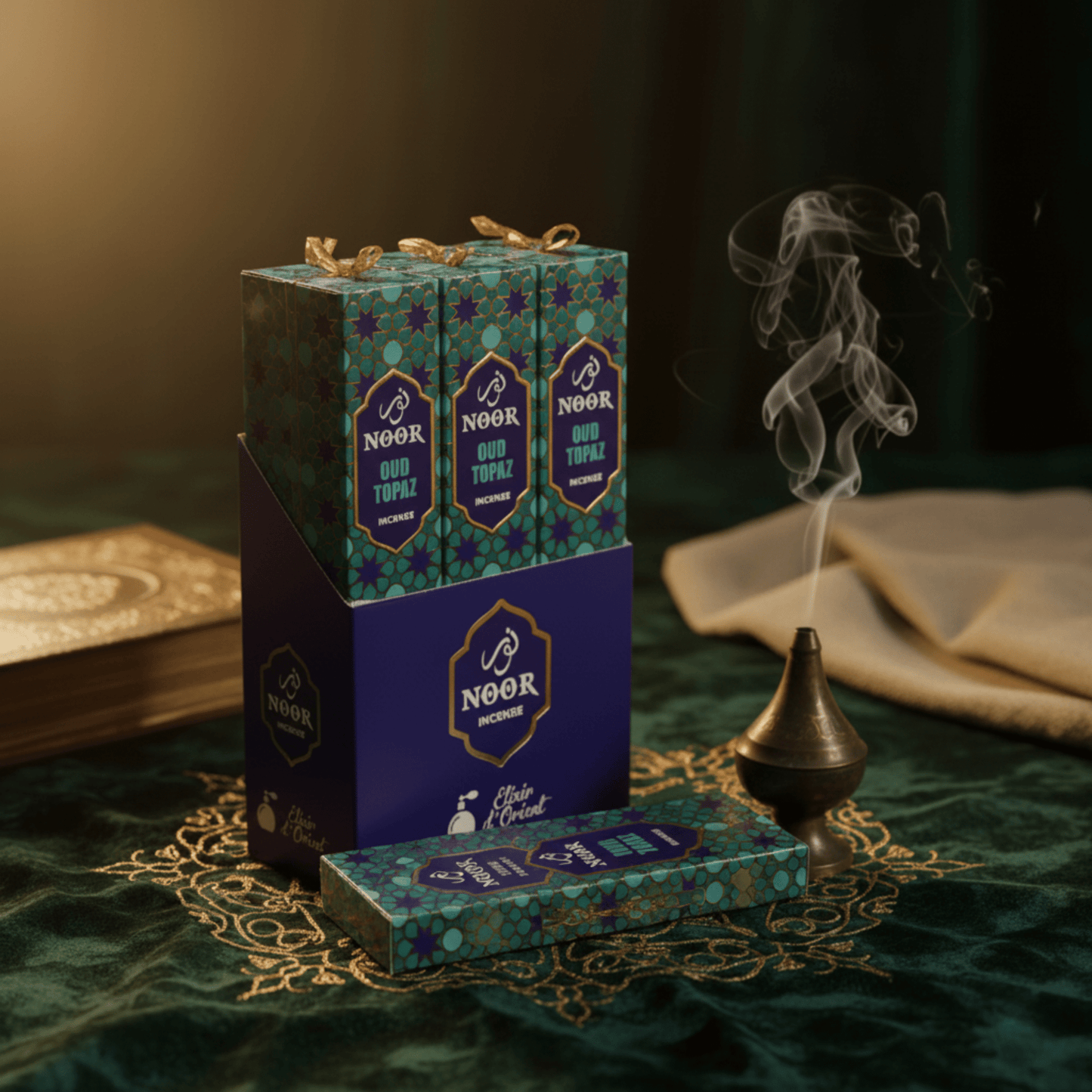 Boîte d’encens Noor Oud Topaz avec fumée parfumée, ambiance orientale luxueuse sur tissu brodé.