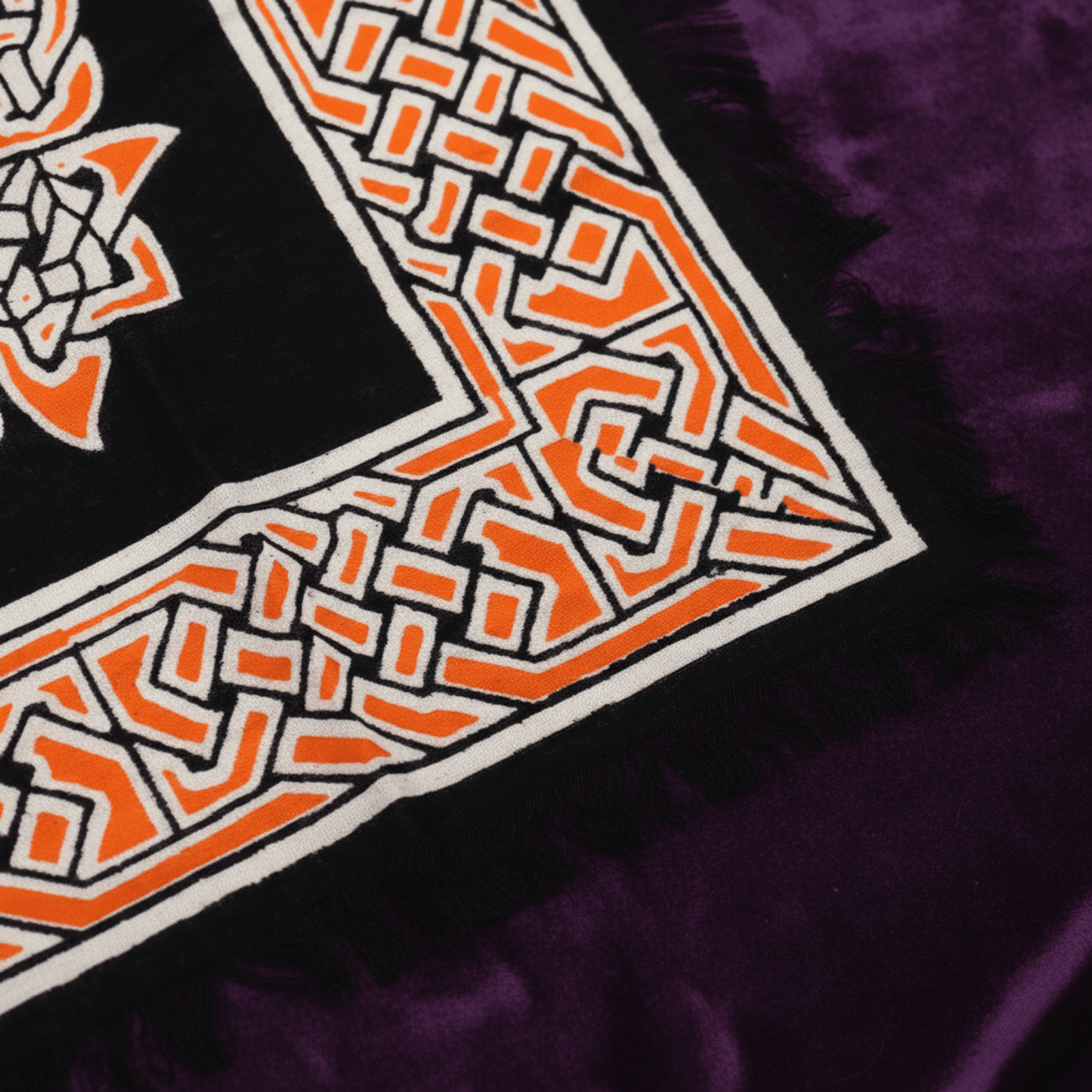 Gros plan sur les motifs celtiques orange et blancs de la nappe Terre Mère, tissu frangé pour autel wicca.