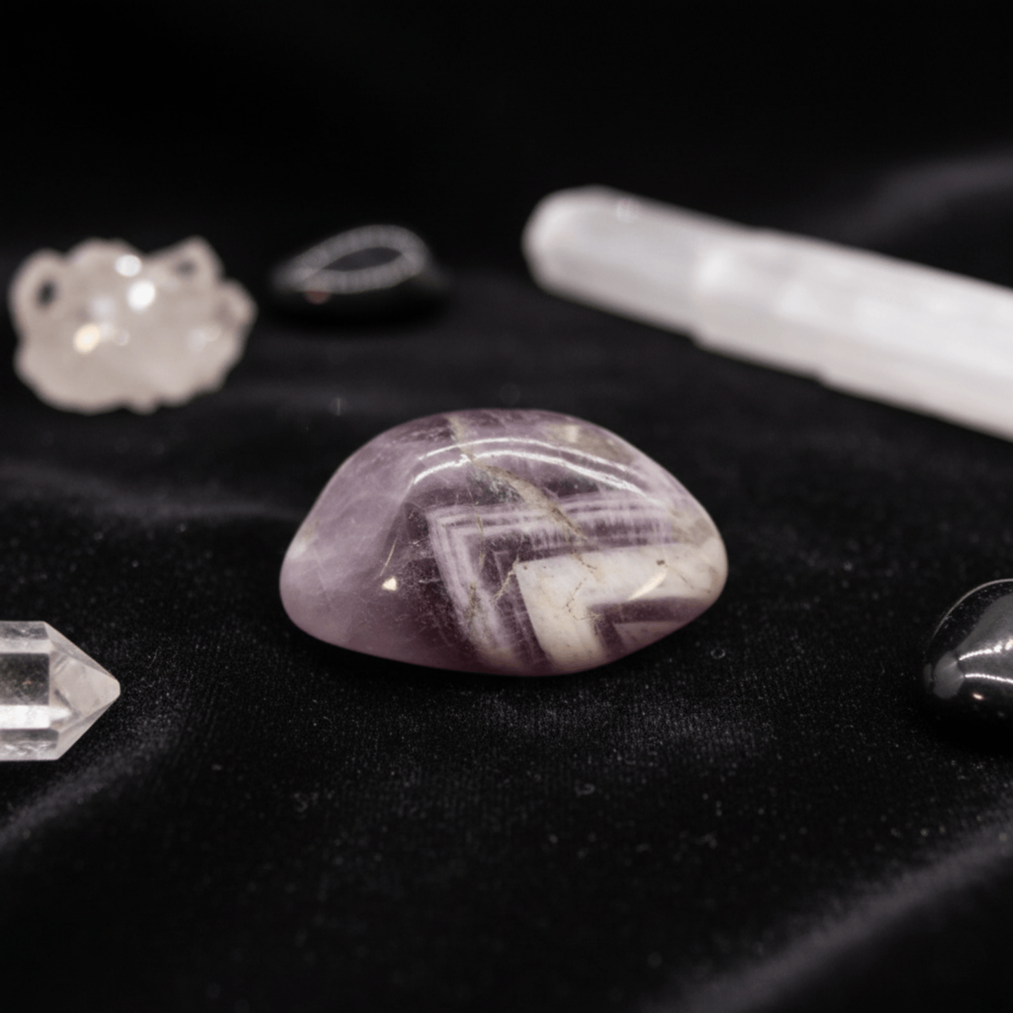 Pierre roulée d’améthyste violette sur tissu noir, entourée de cristaux de quartz et outils de purification énergétique.
