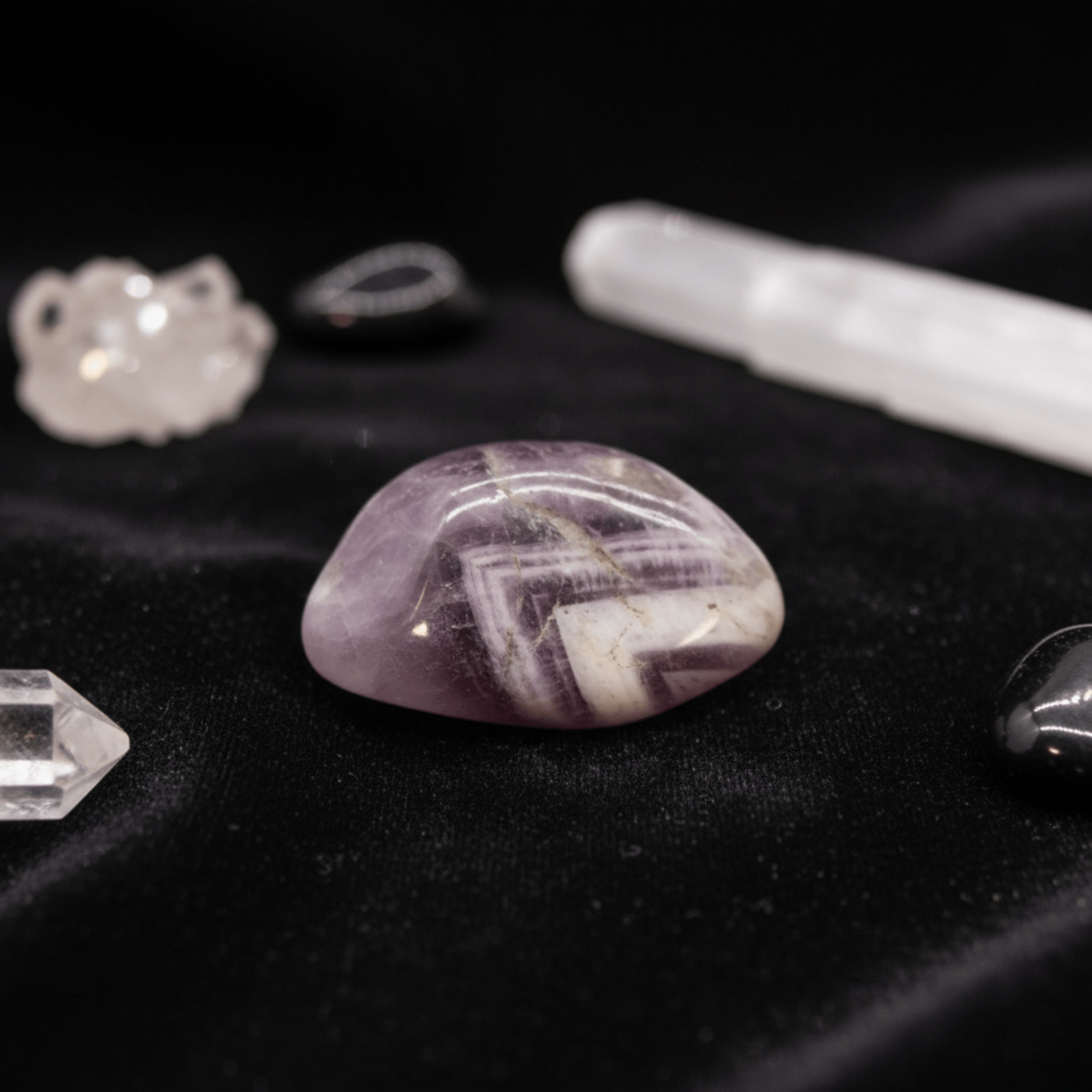 Pierre roulée d’améthyste violette sur tissu noir, entourée de cristaux de quartz et outils de purification énergétique.