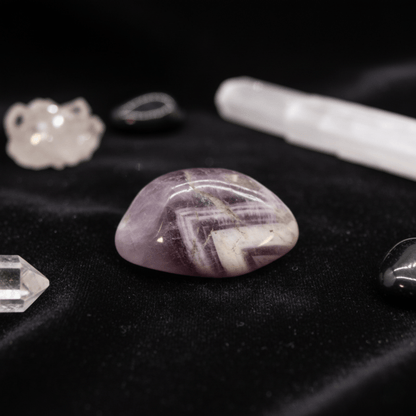 Pierre roulée d’améthyste violette sur tissu noir, entourée de cristaux de quartz et outils de purification énergétique.