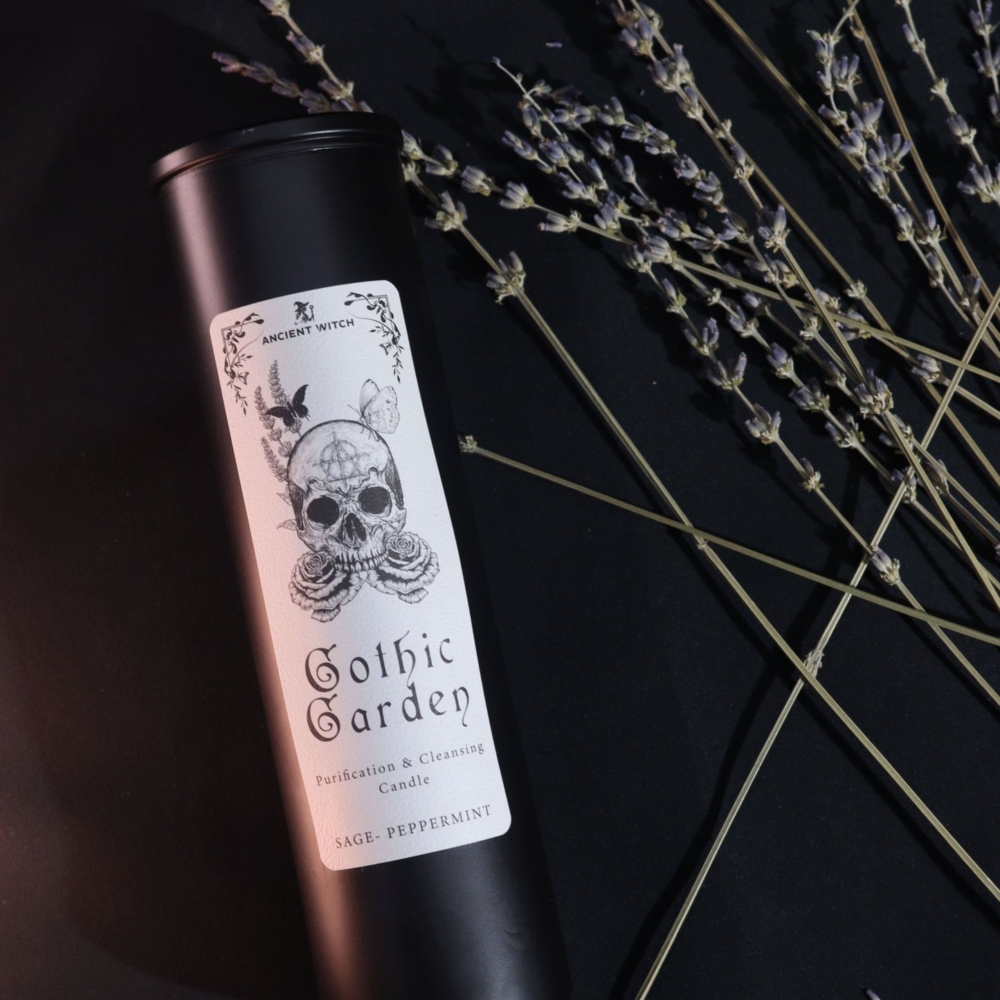 Bougie Gothic Garden noire avec étiquette crâne et roses, parfum sauge-menthe, posée près de branches de lavande.