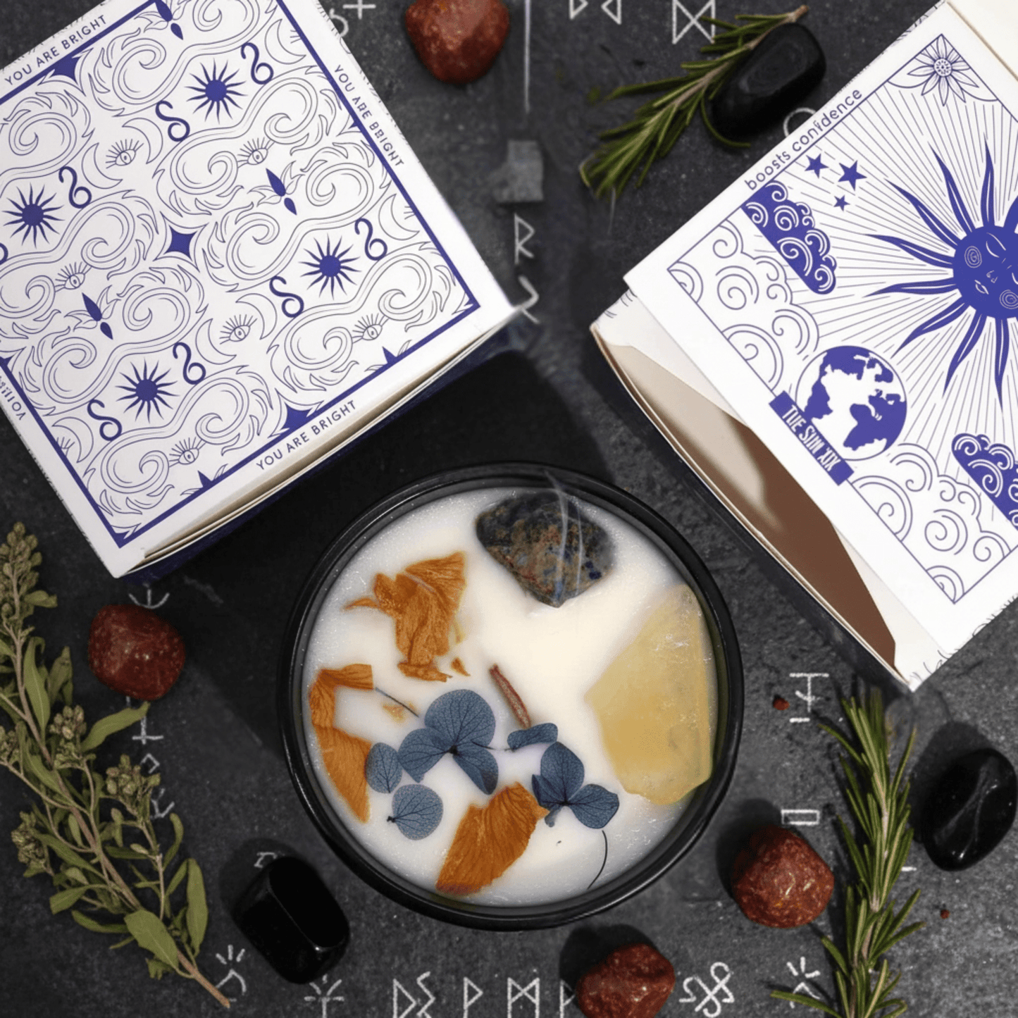 Vue dessus bougie solaire citrine–sodalite Hop Hare, décor fleurs séchées et packaging ésotérique entouré de runes.