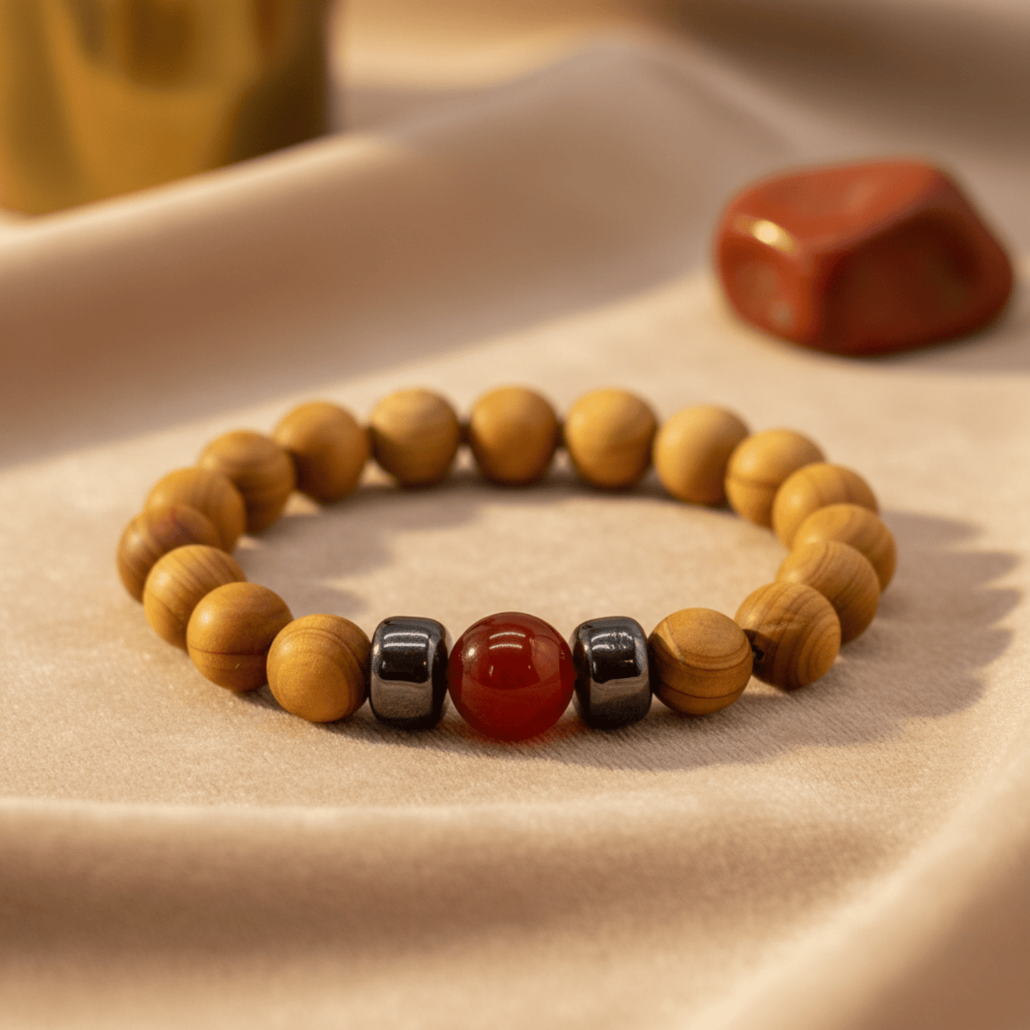 Bracelet en bois de cèdre avec perle de jaspe rouge posé sur tissu beige, pierre jaspe en arrière-plan.