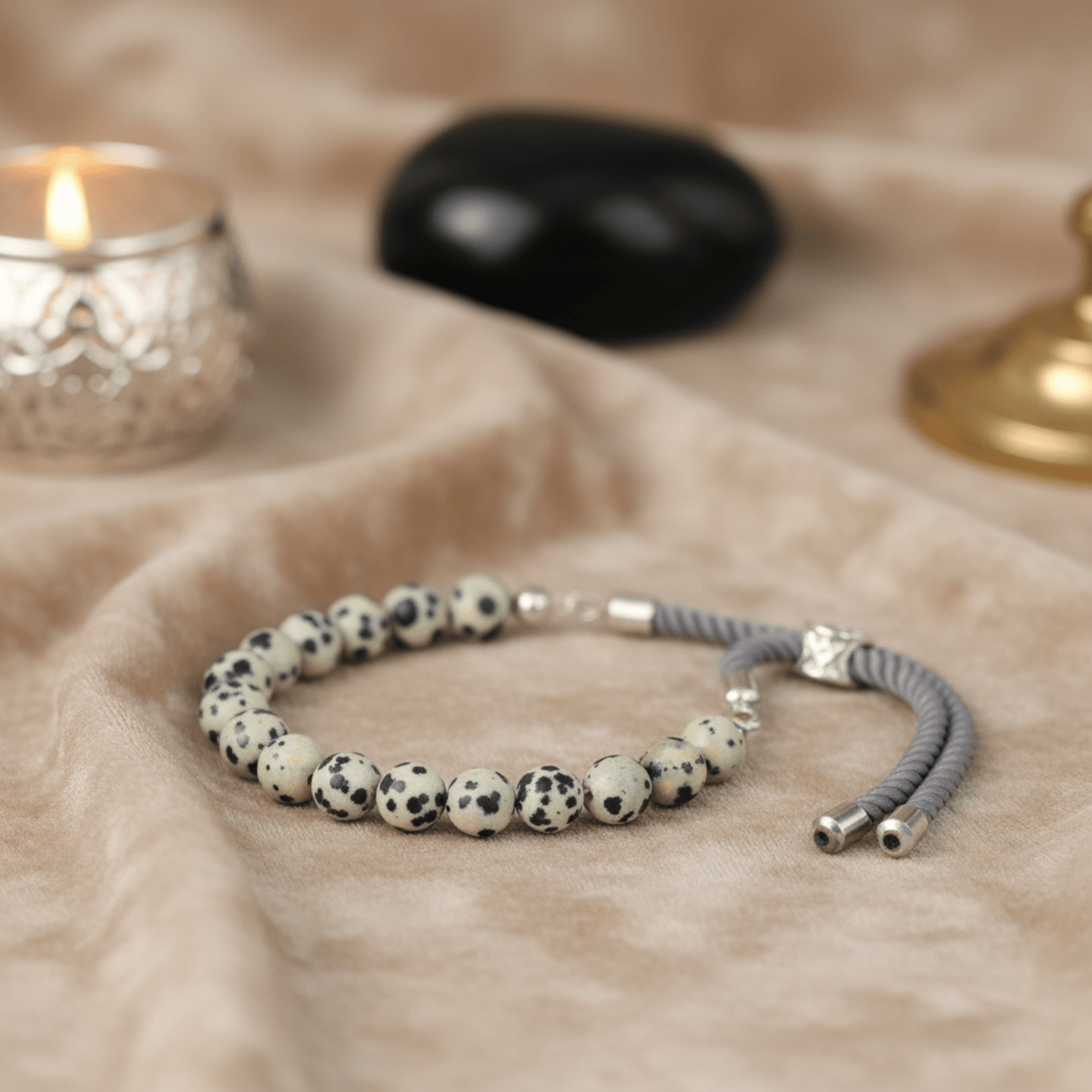 Bracelet en perles Jaspe Dalmatien et cordon gris, finition argent 925, exposé sur tissu beige ambiance lithothérapie.