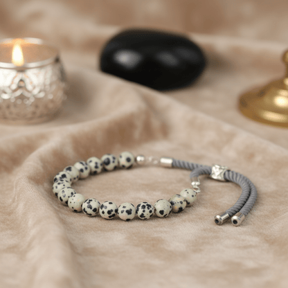 Bracelet en perles Jaspe Dalmatien et cordon gris, finition argent 925, exposé sur tissu beige ambiance lithothérapie.