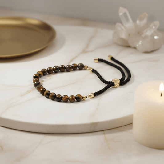 Bracelet œil de tigre naturel avec cordon noir et finitions or 18K posé sur marbre, bijou protection et confiance.