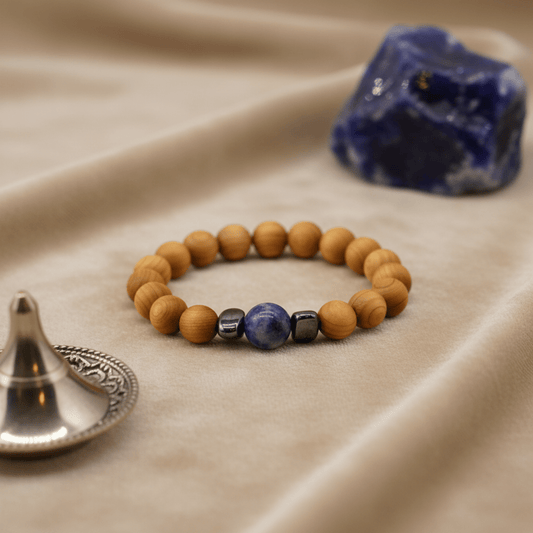 Bracelet en bois de cèdre et perle de sodalite posé sur tissu beige, avec pierre bleue en arrière-plan.