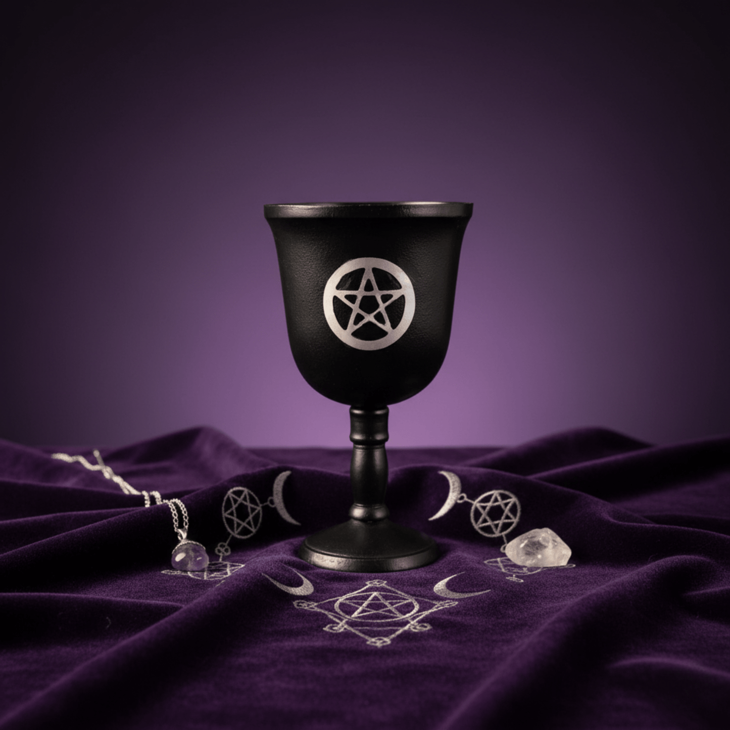 Calice pentacle noir pour rituels wiccans, exposé sur tissu violet avec symboles ésotériques et cristaux.