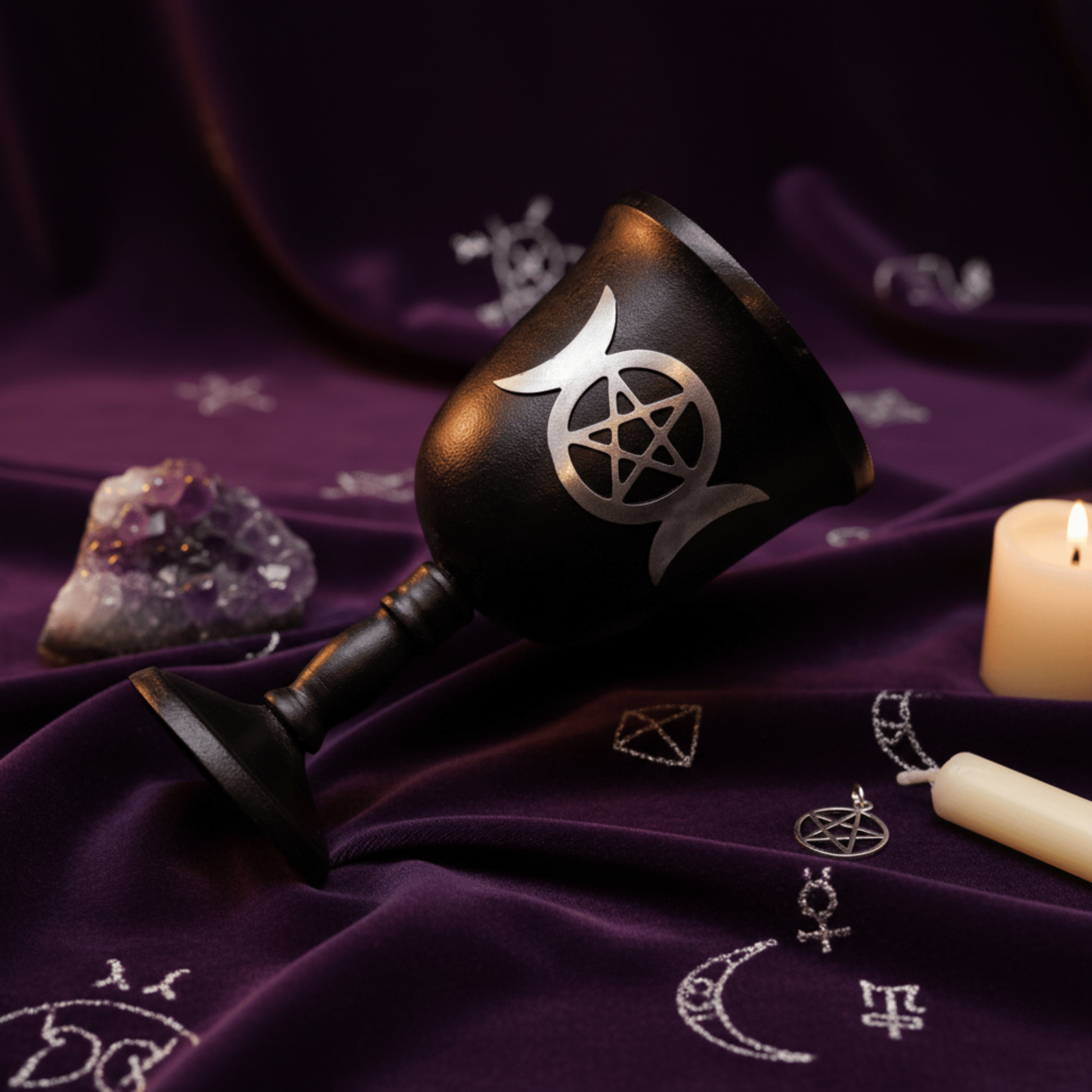 Calice Triple Lune en fer noir couché sur tissu violet, entouré d’améthyste et d’une bougie.