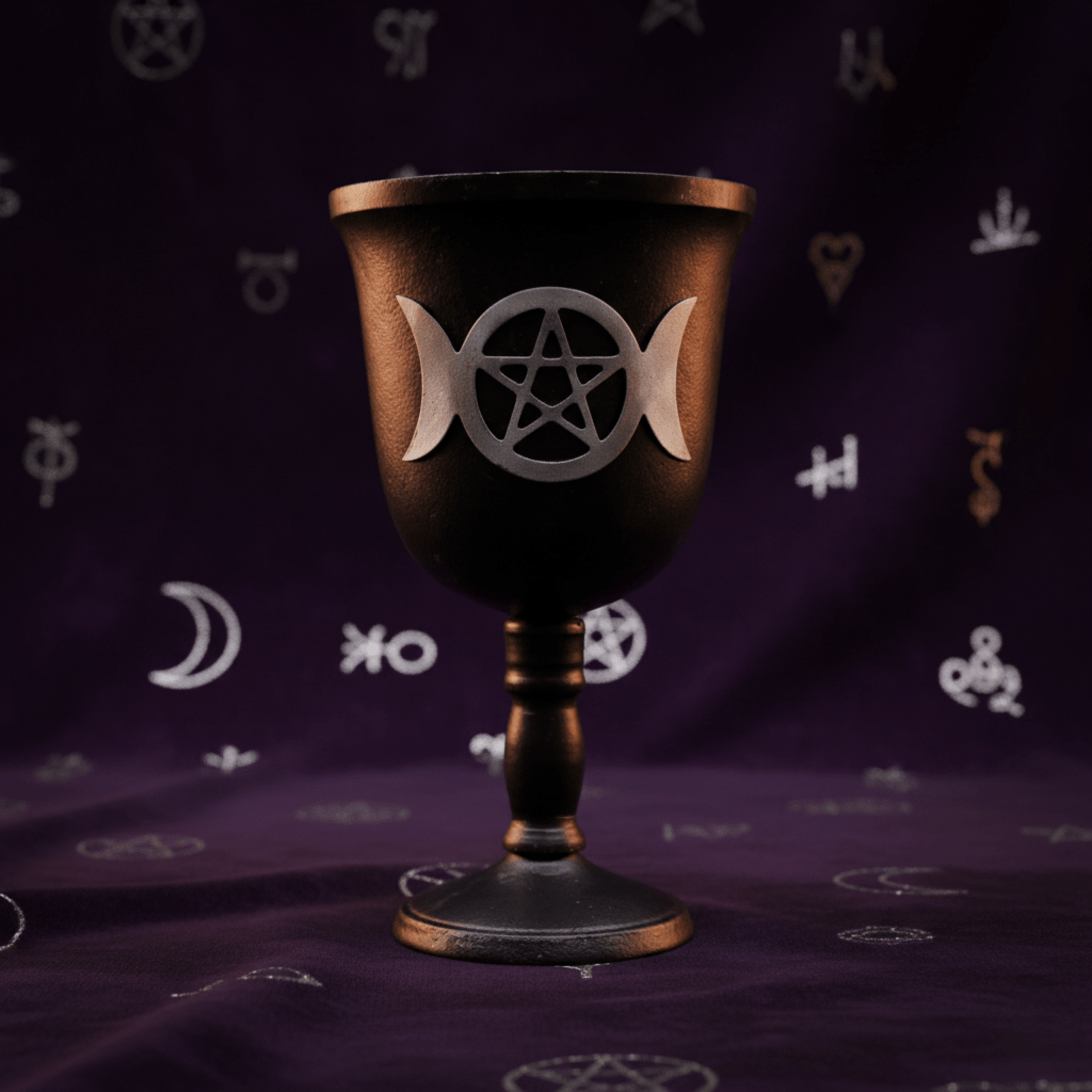 Calice rituel en fer noir avec symbole Triple Lune et pentacle, posé sur tissu violet ésotérique.