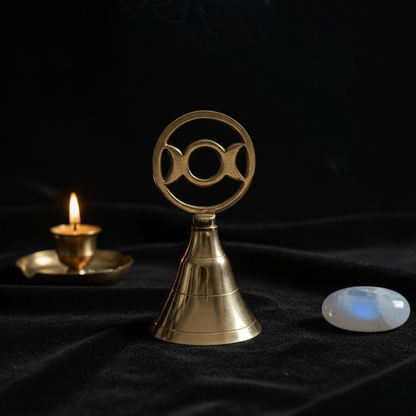 Cloche rituelle en laiton Triple Lune sur autel wiccan, avec bougie et pierre de lune.