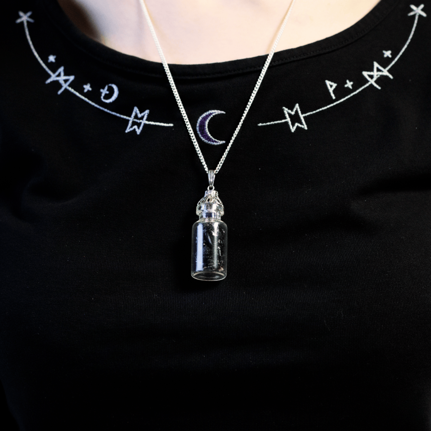 Collier bouteille d’onyx noir porté autour du cou sur un haut noir à motifs mystiques.