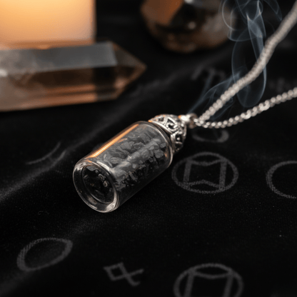 Collier bouteille d’onyx noir sur tissu noir rituel avec cristaux et fumée en arrière-plan.
