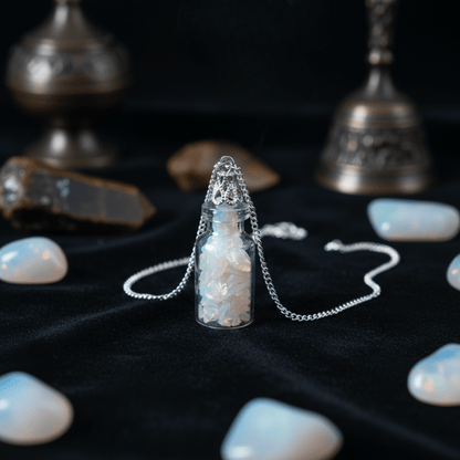 Collier bouteille/fiole opalite avec gemmes iridescentes posé sur tissu noir, bijou ésotérique lumineux.