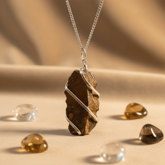 Collier Œil de Tigre brut enveloppé de fil argenté, pendentif pierre naturelle énergétique posé sur tissu beige.