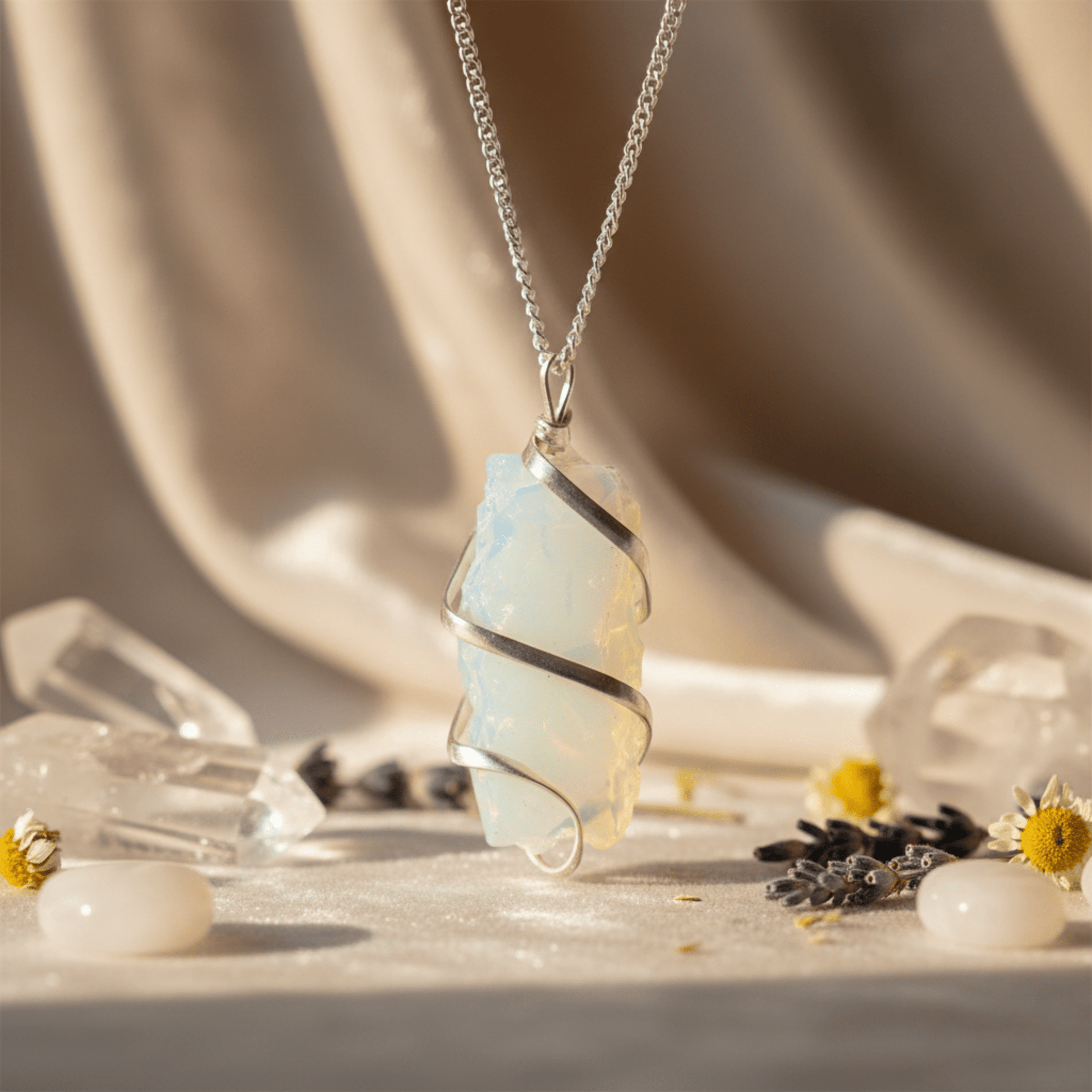 Pendentif en opalite brute enveloppée de fil argenté sur chaîne, éclairé par une lumière douce avec cristaux en arrière-plan.