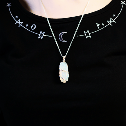 Collier en opalite brute porté autour du cou, pendentif lumineux mis en valeur sur un haut noir décoré de symboles mystiques.