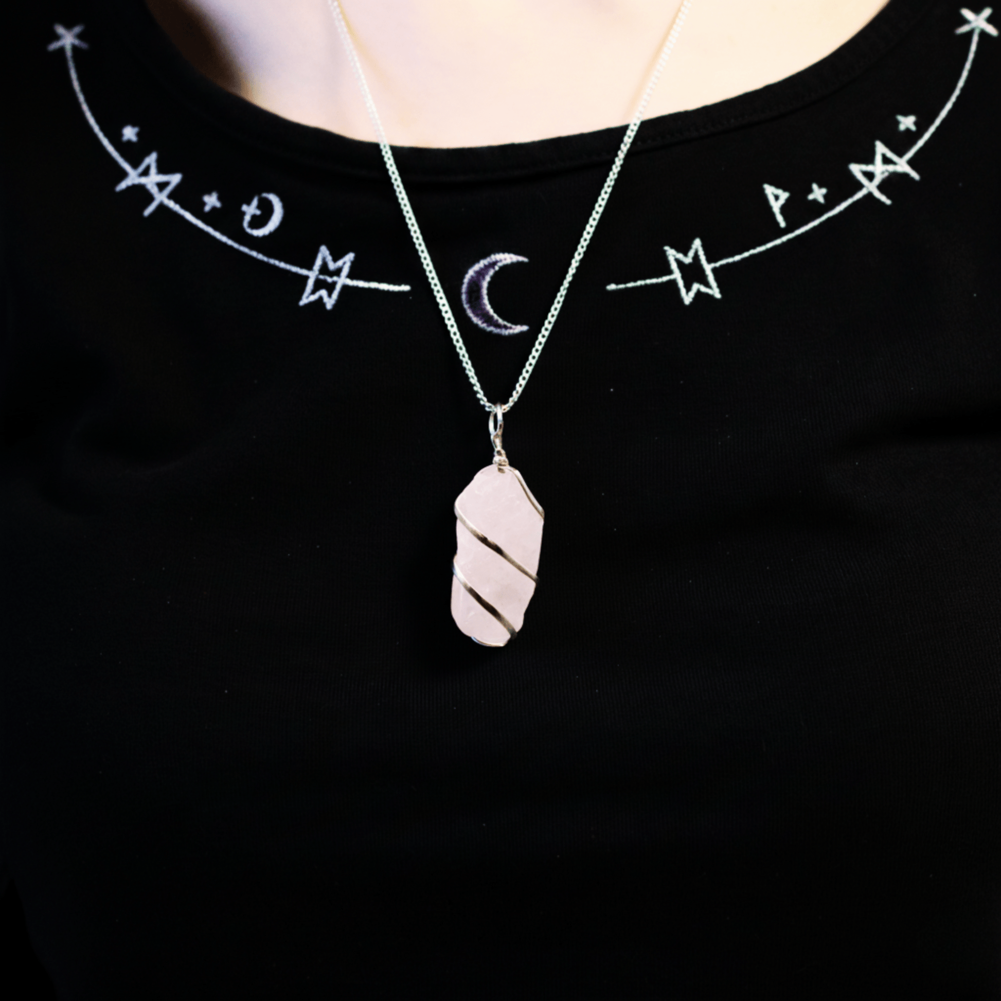 Collier quartz rose brut porté sur poitrine, pendentif en fil argenté mis en valeur sur vêtement noir mystique.