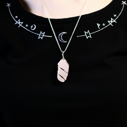 Collier quartz rose brut porté sur poitrine, pendentif en fil argenté mis en valeur sur vêtement noir mystique.