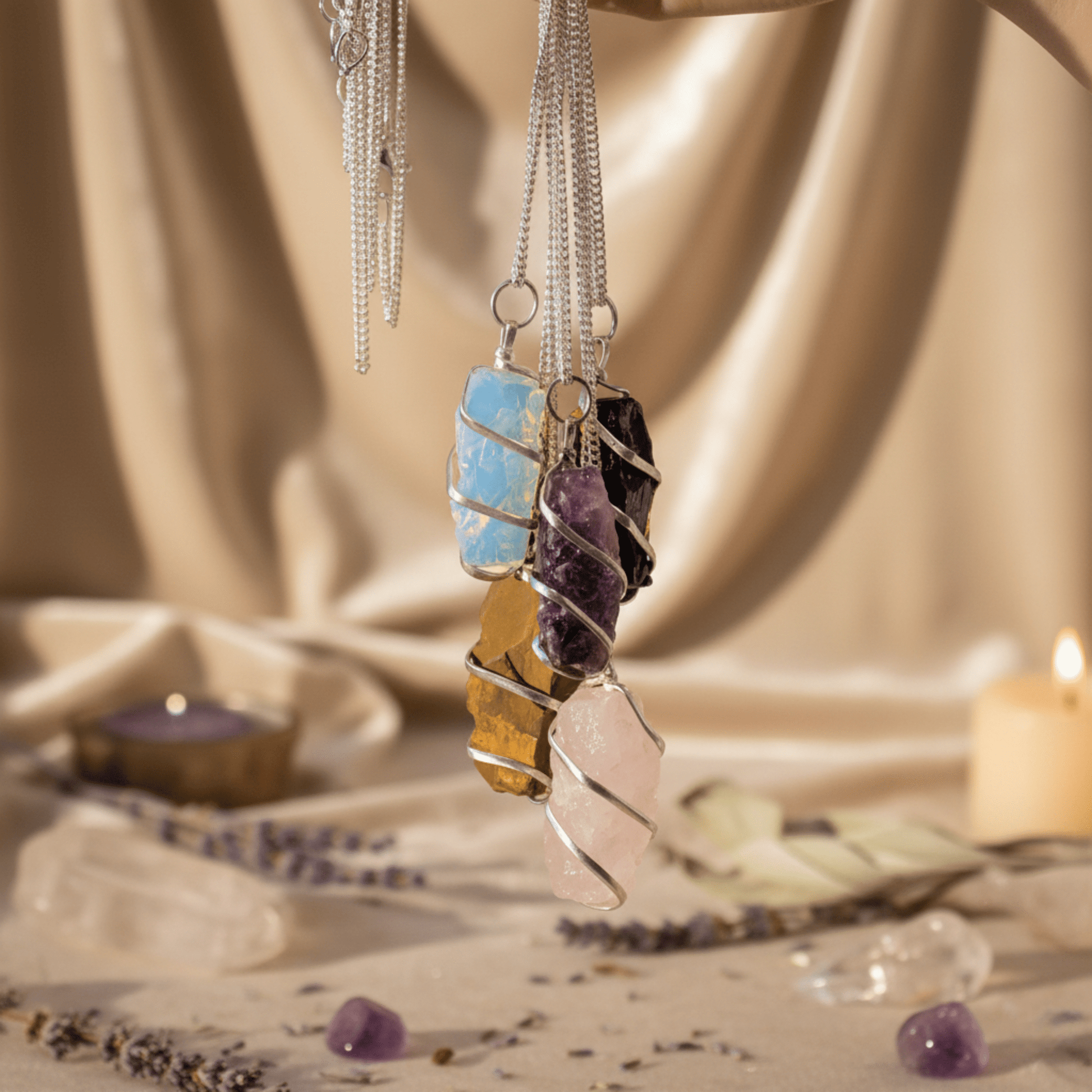 Collection de pendentifs en pierres naturelles brutes, dont quartz rose, suspendus dans ambiance spirituelle.