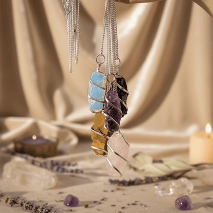 Collection de pendentifs en pierres naturelles brutes, dont quartz rose, suspendus dans ambiance spirituelle.