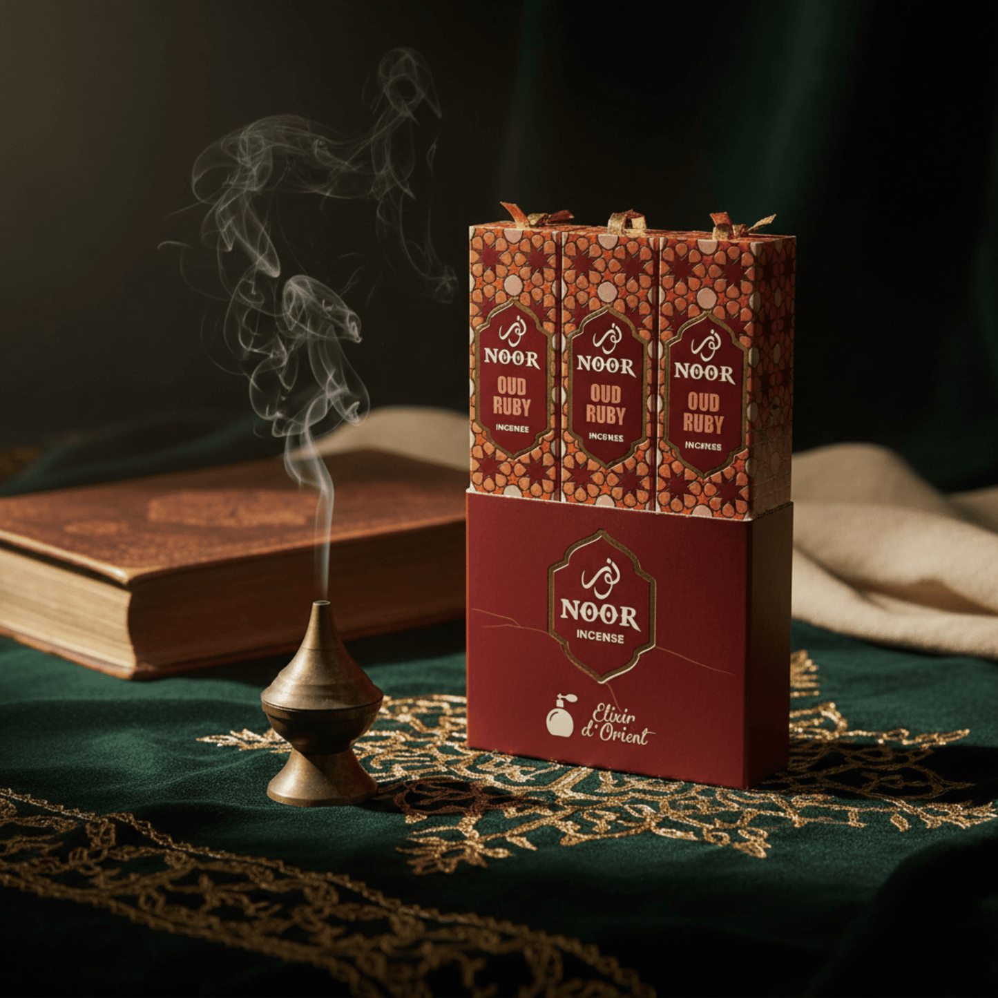 Boîte d’encens Noor Ruby avec fumée mystique, ambiance orientale et tissu vert doré luxueux.