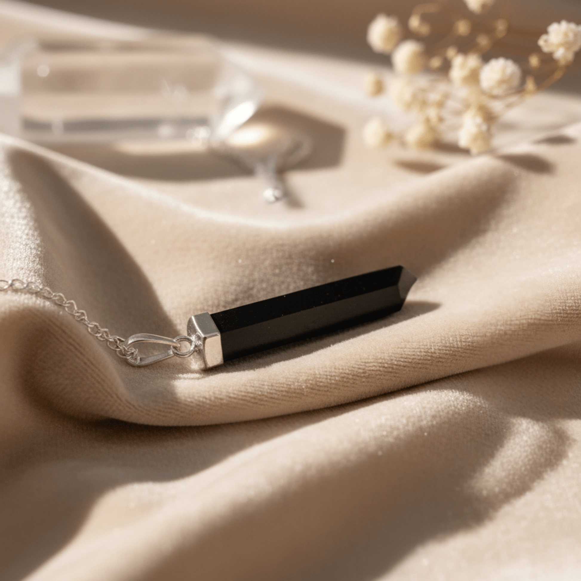 Collier pointe en Agate Noire allongé sur tissu clair, bijou énergétique naturel.