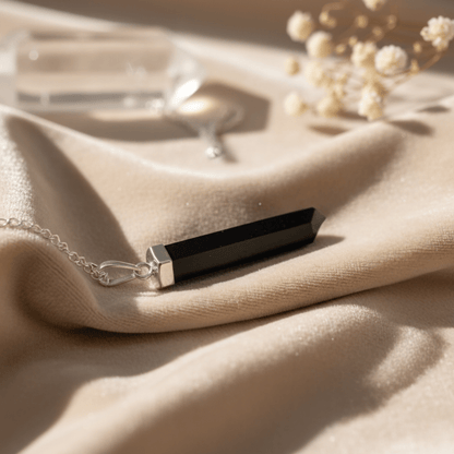 Collier pointe en Agate Noire allongé sur tissu clair, bijou énergétique naturel.