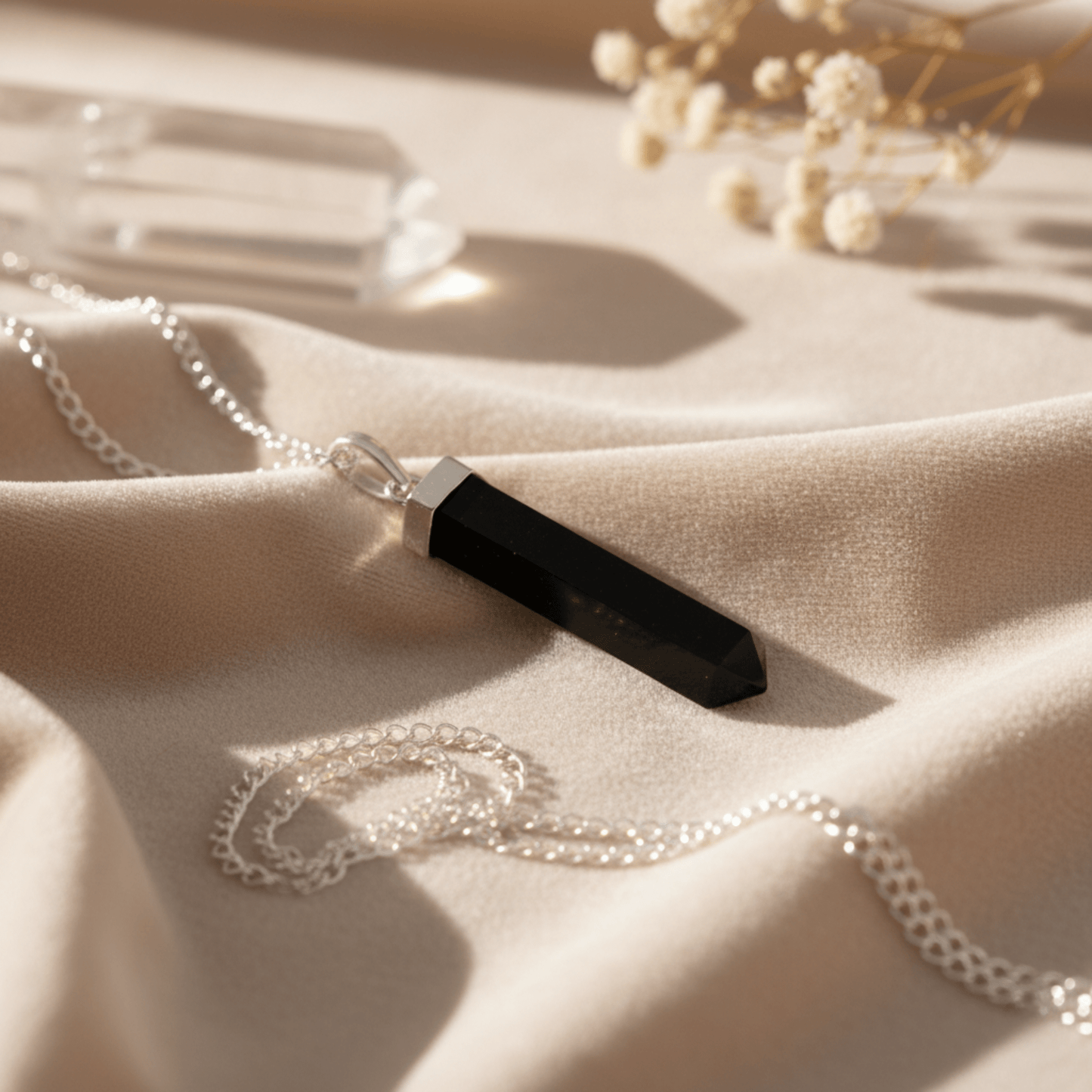 Collier pointe en Agate Noire posé sur tissu beige, pierre naturelle d’ancrage.