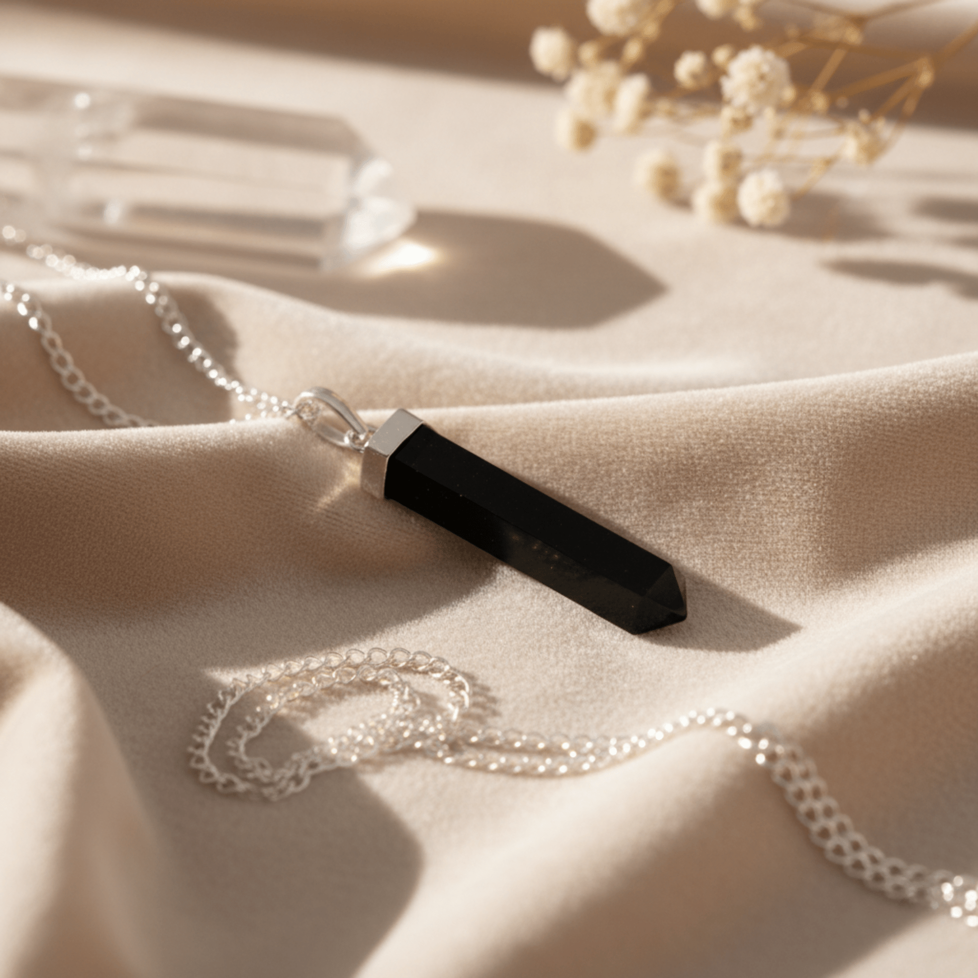 Collier pointe en Agate Noire posé sur tissu beige, pierre naturelle d’ancrage.