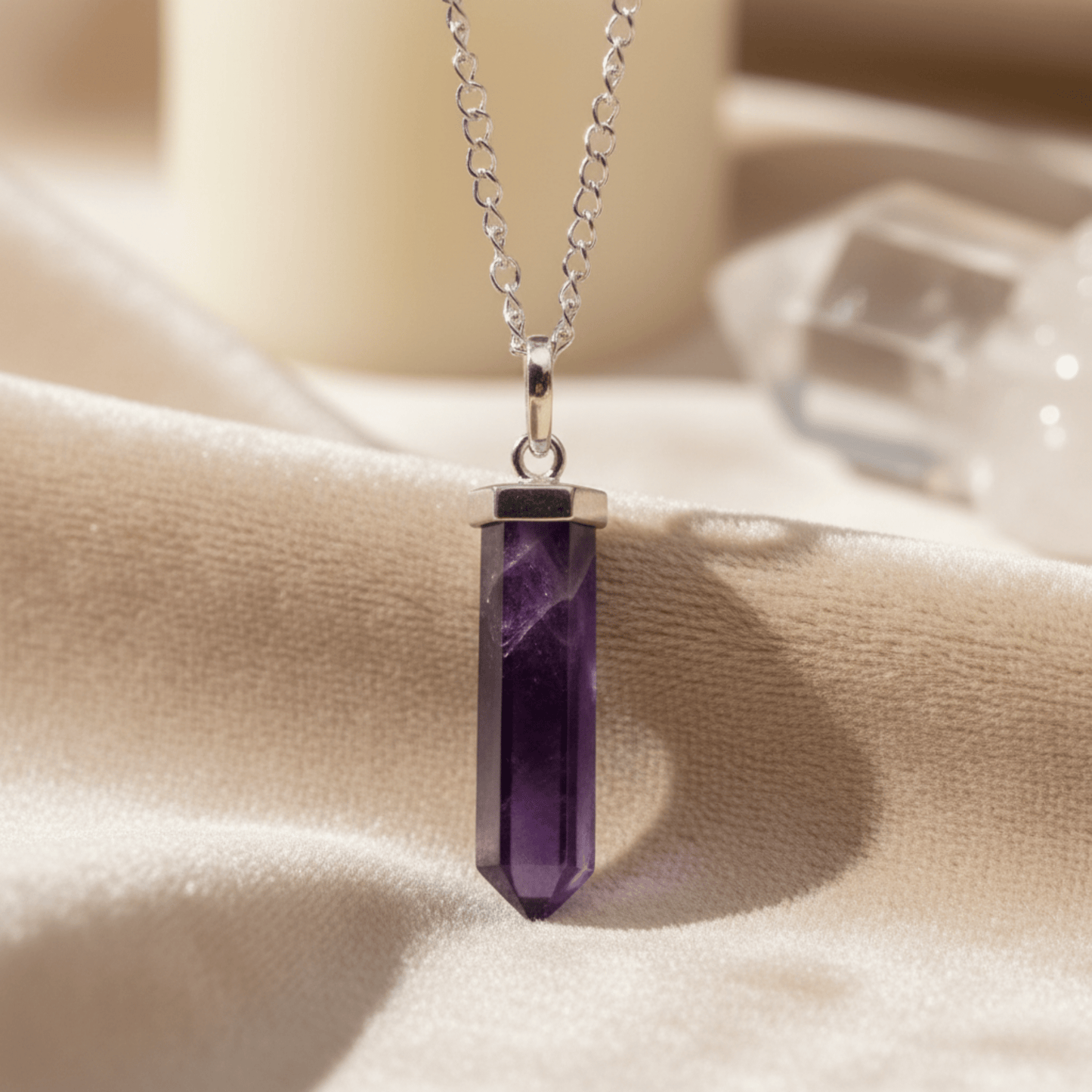 Pointe d’améthyste en pendentif argenté sur tissu clair, pierre violette naturelle énergétique.