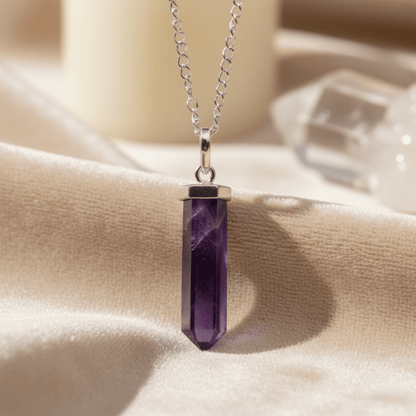 Pointe d’améthyste en pendentif argenté sur tissu clair, pierre violette naturelle énergétique.