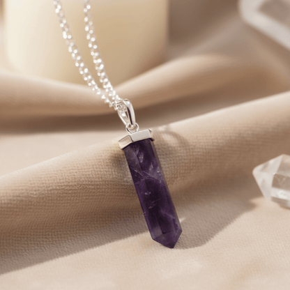 Pendentif en améthyste posé sur tissu beige, pierre violette naturelle pour apaisement et intuition.