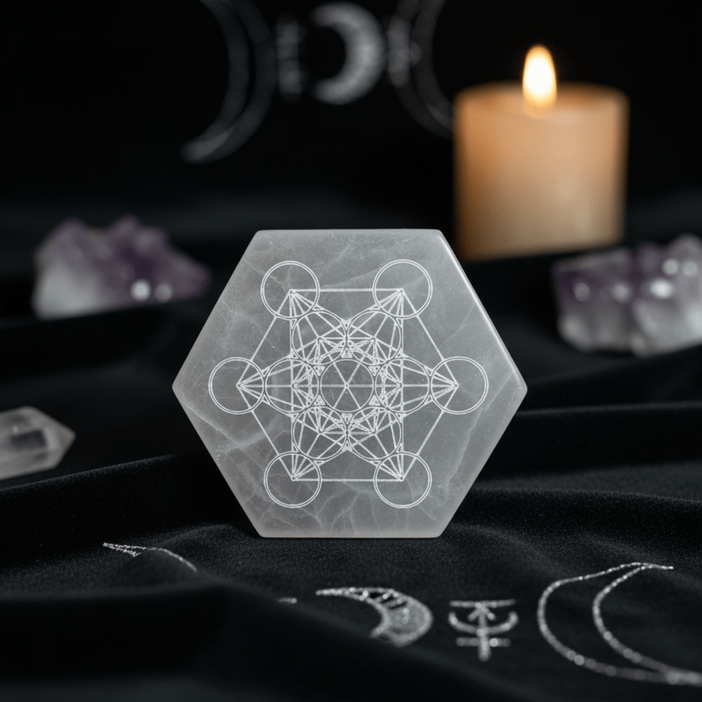 Plaque hexagonale en sélénite gravée du Cube de Métatron sur tissu noir, avec bougie et cristaux.