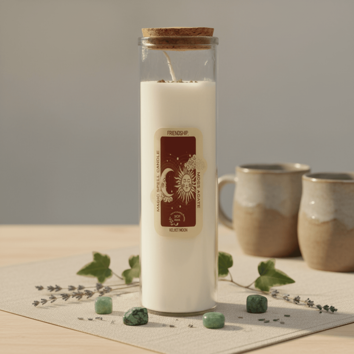 Bougie rituel Amitié avec pierres de moss agate et symbole soleil-lune, décor wicca et tasses en arrière-plan.