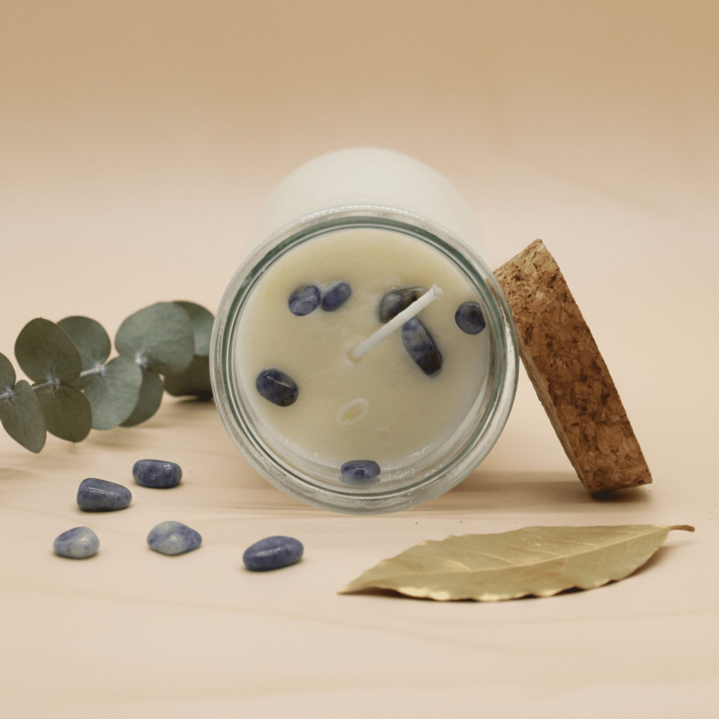 Bougie rituelle avec pierres bleues sodalite incrustées, posée avec feuilles d’eucalyptus et laurier.