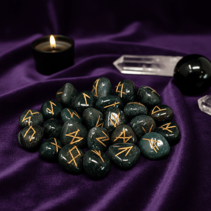 Runes en héliotrope pour tirage divinatoire, pierres vertes gravées or sur tissu violet rituel.